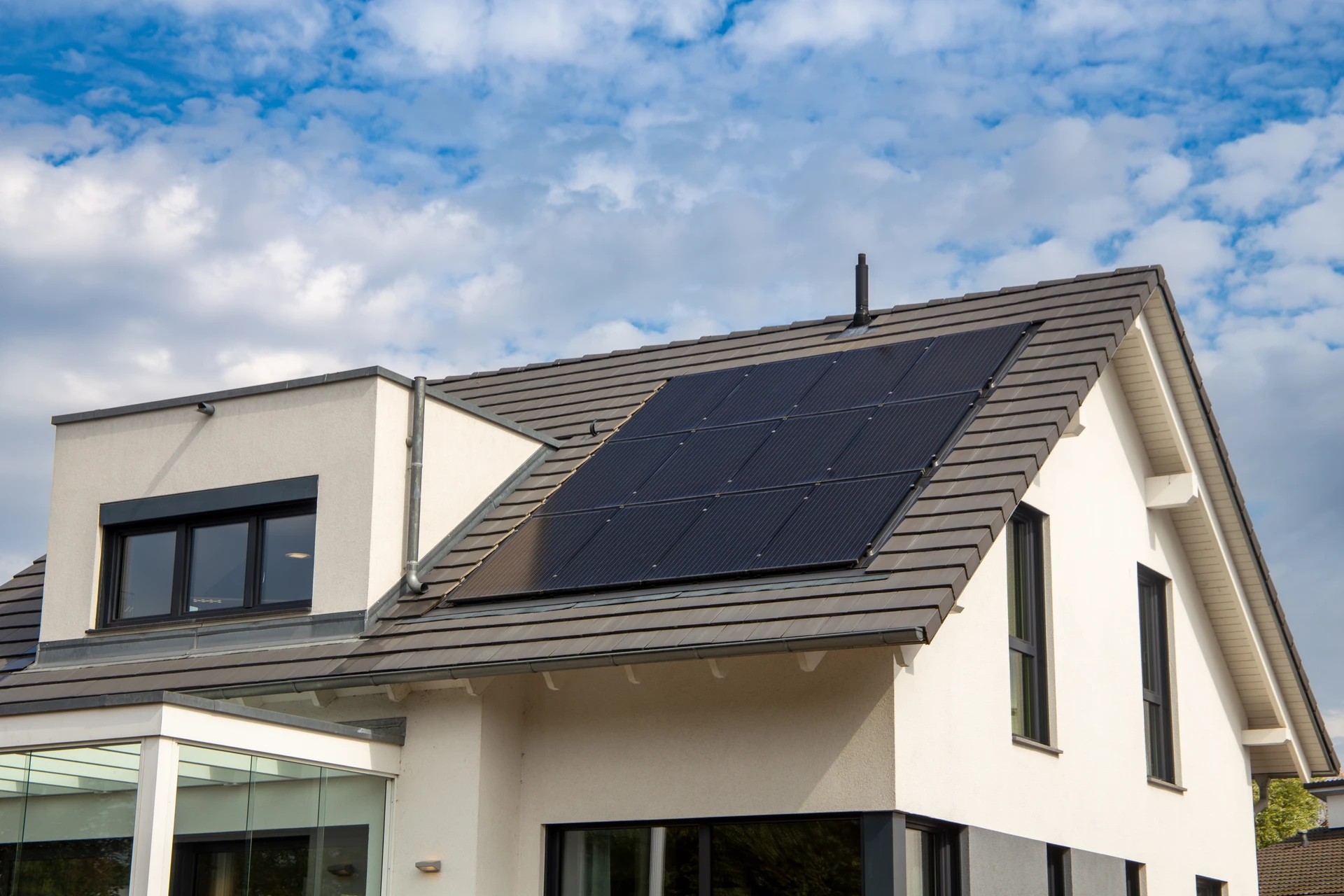 Technicien en tenue de travail professionnelle installant un panneau solaire photovoltaïque noir monocristallin sur une toiture en tuiles canal terre cuite, fixation par rails aluminium et pinces de serrage inox, cellules PERC demi-format visibles, environnement résidentiel ensoleillé.