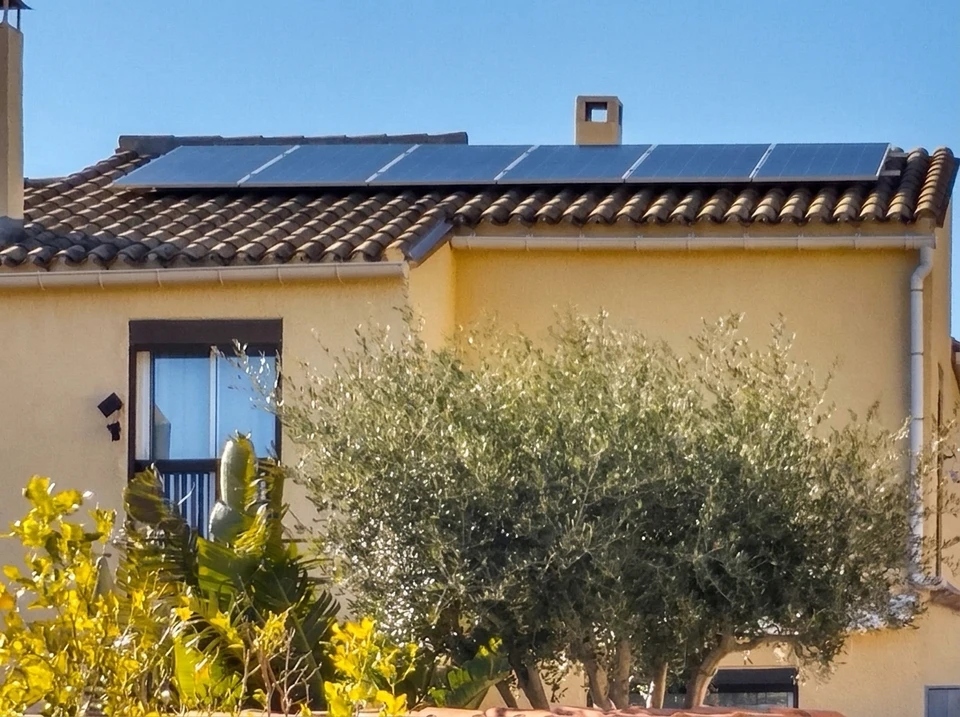 Toiture en tuiles canal avec panneaux solaires photovoltaïques intégrés, vue en contre-plongée sous ciel nuageux